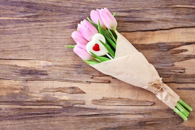 Beautiful pink tulips in paper with sweet heart on wooden background