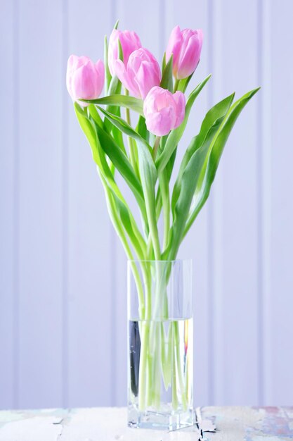 Beautiful pink tulips in vase on table on wooden background