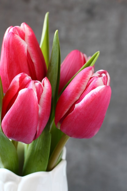 Beautiful pink tulips in white vase on wooden background