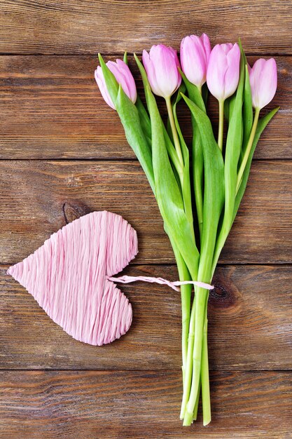 Beautiful pink tulips with decorative heart on wooden background