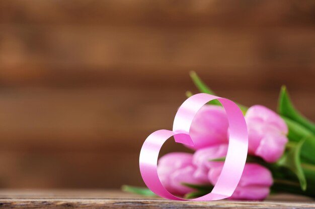 Beautiful pink tulips with decorative heart on wooden background