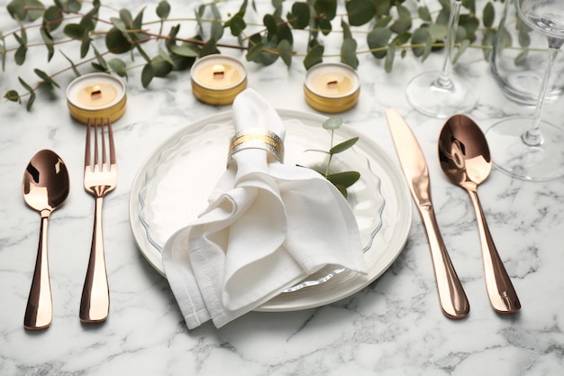 Beautiful place setting with candles and eucalyptus on white marble table