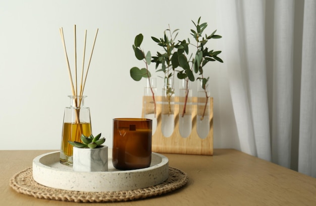 Beautiful plant candle and aromatic reed air freshener on wooden table indoors space for text Interior elements