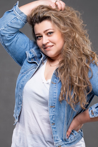 A beautiful plump girl in denim clothes looks at the camera and smiles.
