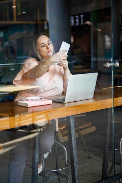 Beautiful plus size business woman posing taking selfie use smartphone working remotely at cafe