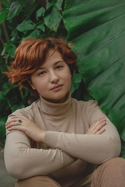 Photo a beautiful plus size girl with red hair among the lush green branches of tropical plants