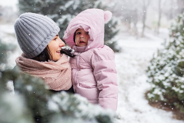 Beautiful portrait of happy smile mother with her toddler girl outdoors in park or forest on snowing dayWinter mood Family portrait Motherhood and childhood