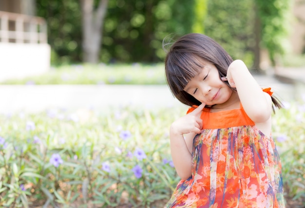 Красивый портрет маленькая девочка Азии улыбается стоя на зеленой траве в парке.