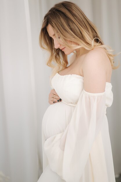 완벽한 임신 여성의 흰색 드레스 개념에 임신한 여자의 아름다운 초상화는 그녀의 손을 넣어