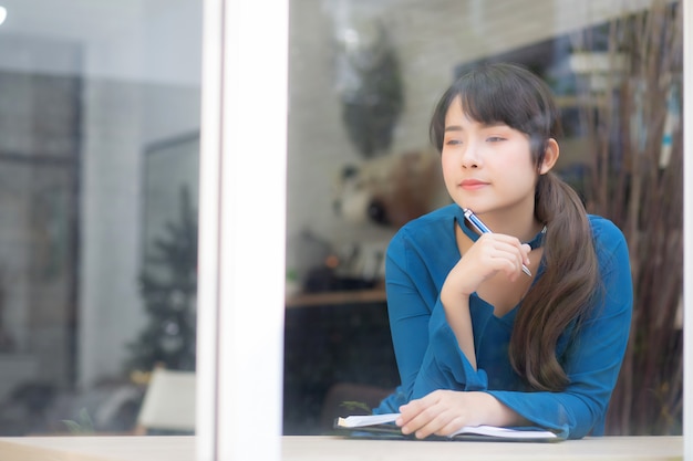 Beautiful portrait young asian woman writer smiling thinking idea and writing on notebook