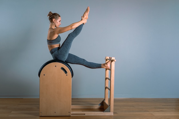 Beautiful positive blond woman performing pilates exercise, training on barrel equipment.