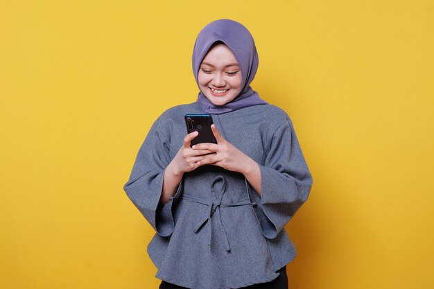 Beautiful positive friendly-looking young woman wearing hijab with lovely sincere smile feeling thankful and grateful holding mobile phone