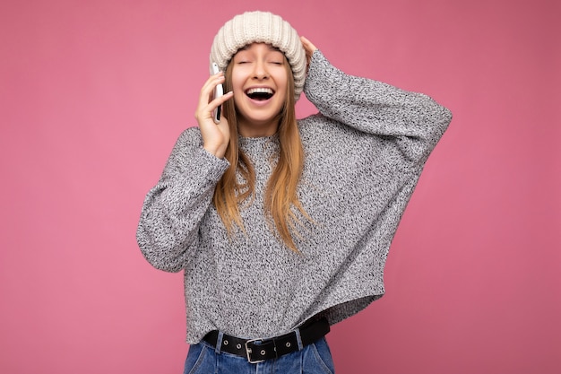 Beautiful positive happy young blonde woman wearing casual grey sweater and beige hat