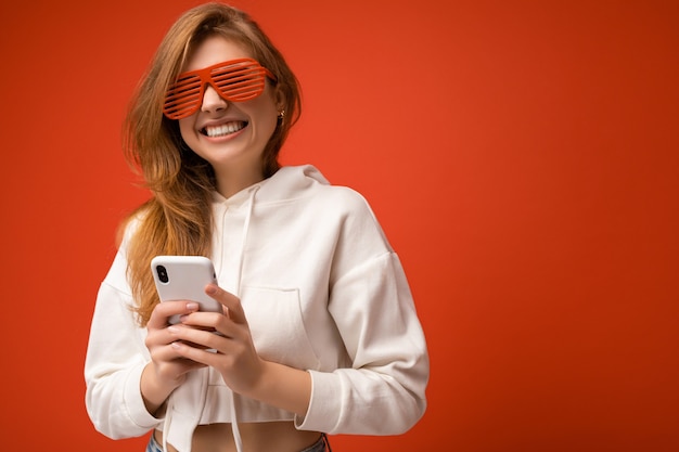 Beautiful positive young blonde woman wearing stylish white hoodie and funny colorful glasses