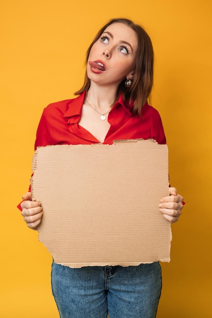 A beautiful positive young Caucasian woman is holding an empty banner on a yellow background Copying space