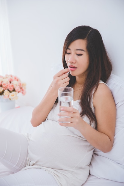 Bella donna asiatica incinta che tiene un bicchiere d'acqua