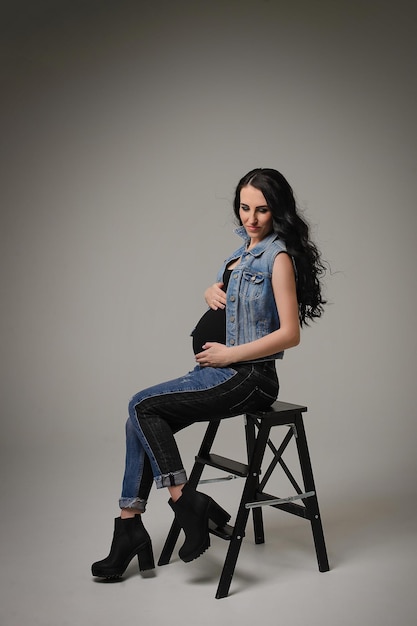 A beautiful pregnant girl in denim clothes on a gray background