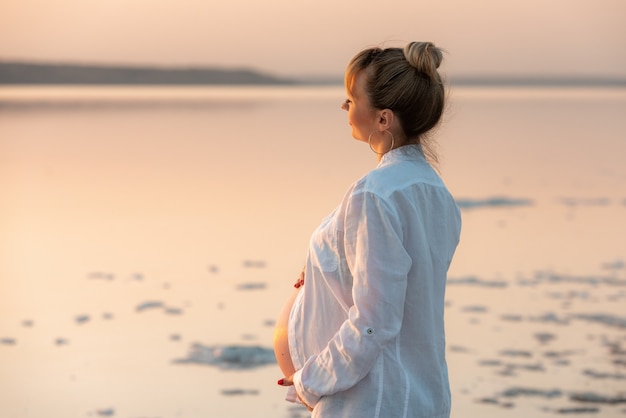 美しい妊娠中の女の子は夕日の光線を楽しんでいます。女性の休息とリラクゼーション。優しい瞬間