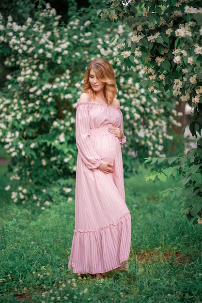 Beautiful pregnant girl in a pink dress outdoors on a background of jasmine