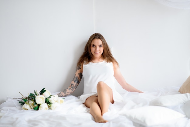 Beautiful pregnant girl in a white dress and with a bouquet of flowers.