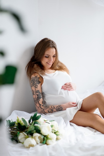 Beautiful pregnant girl in a white dress and with a bouquet of flowers.