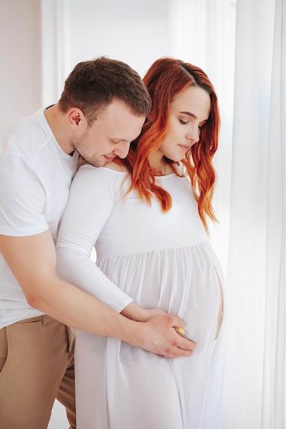 Beautiful pregnant girl in white dress with husband in studio