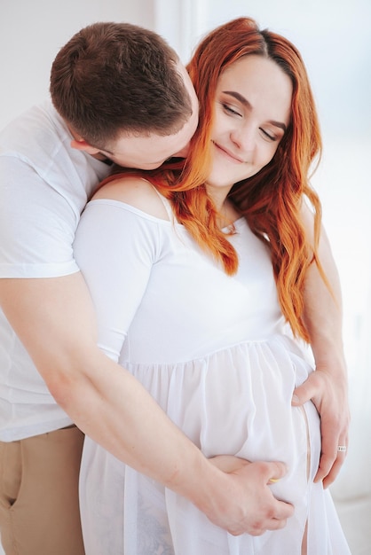 Beautiful pregnant girl in white dress with husband in studio