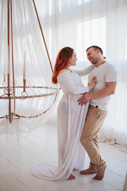 Beautiful pregnant girl in white dress with husband in studio