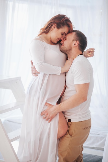 Beautiful pregnant girl in white dress with husband in studio