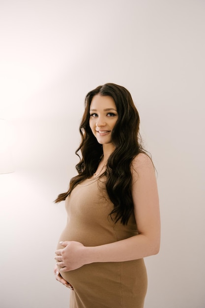 Beautiful pregnant girl with curls in a dress in a bright studio with a stylish interior the concept of a happy pregnancy and family