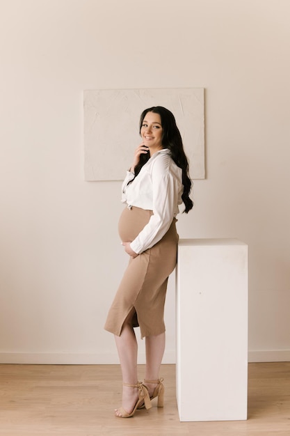 Beautiful pregnant girl with curls in a dress in a bright studio with a stylish interior the concept of a happy pregnancy and family