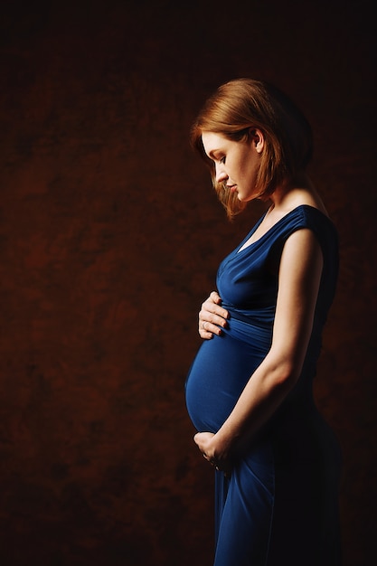 Beautiful pregnant girl with red hair in a blue dress