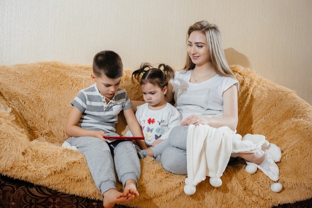 Photo beautiful pregnant mom sitting on the couch with her son and daughter and playing tablet