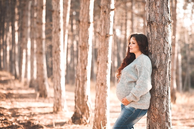 Красивая беременная женщина 30-35 лет в уютном свитере на улице с нетерпением ждет осеннего сезона
