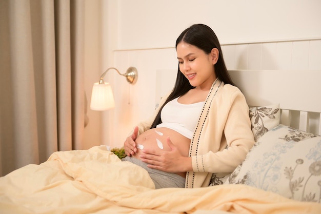 Beautiful pregnant woman applying moisturizing stretch mark cream on belly