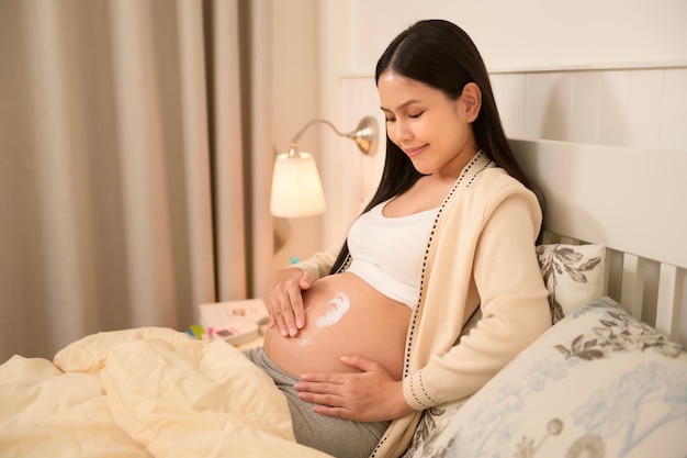 Foto bella donna incinta che applica crema idratante per le stretch mark sulla pancia