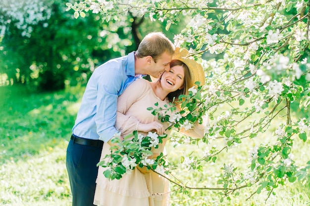 Beautiful pregnant woman in blooming garden. Husband stroking a pregnant belly and they laughing.