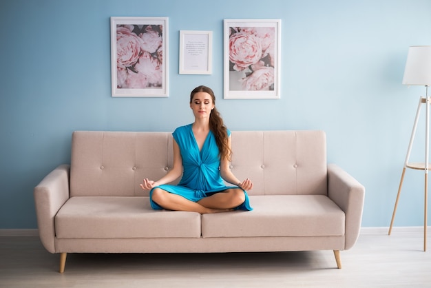 Beautiful pregnant woman in a blue dress is sitting on the sofa.