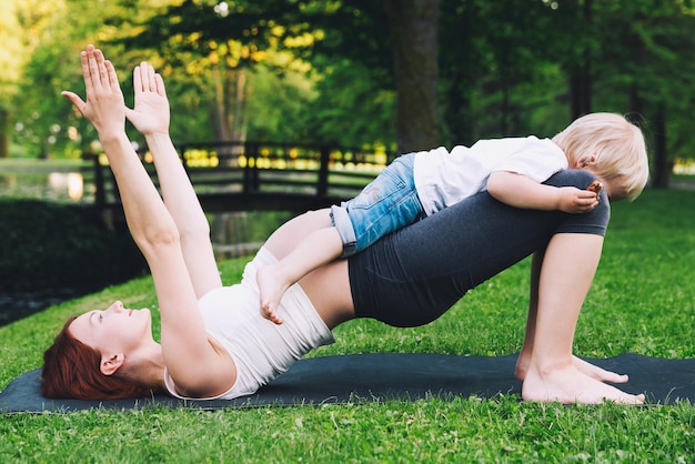 Beautiful pregnant woman doing yoga with little son on nature outdoors Little yogi yoga kids