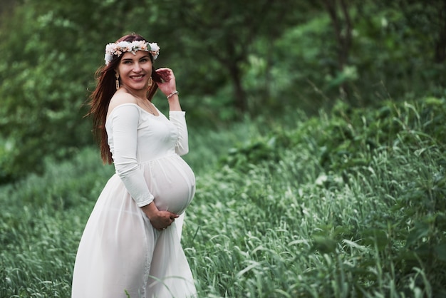 Beautiful pregnant woman in dress have a walk outdoors. Positive brunette