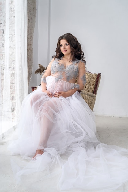 Beautiful pregnant woman in dress posing sitting in armchair