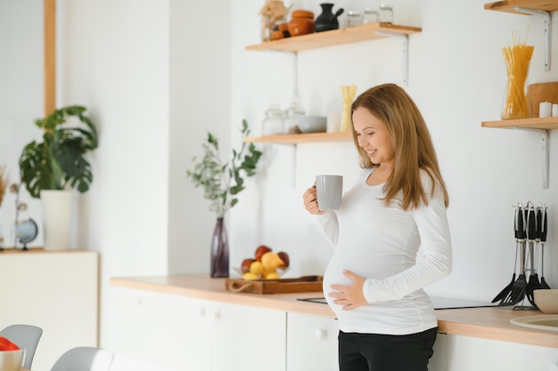 Beautiful pregnant woman drinks tea or coffee. Indoor photo.