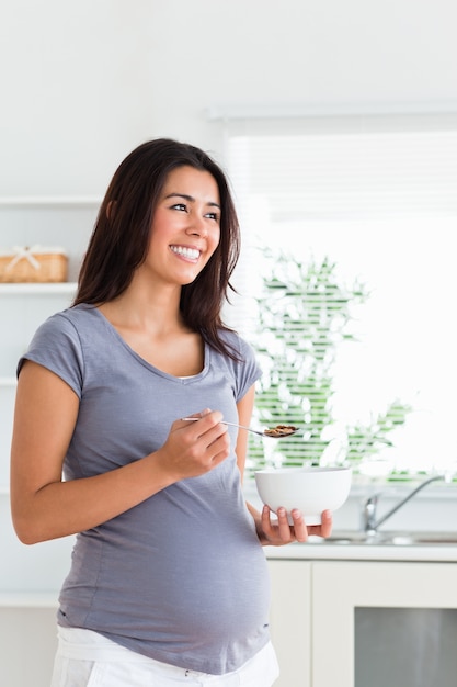 Beautiful pregnant woman enjoying a bowl of cereals while standing