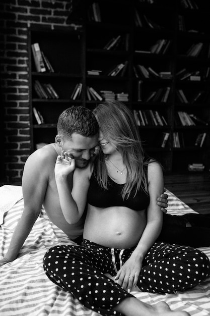 Beautiful pregnant woman and her handsome husband are smiling while spending time together in bed