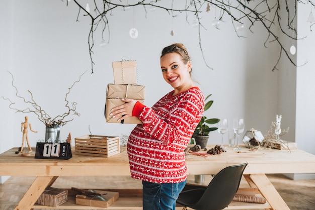 Beautiful pregnant woman holding a bundle of christmas gifts