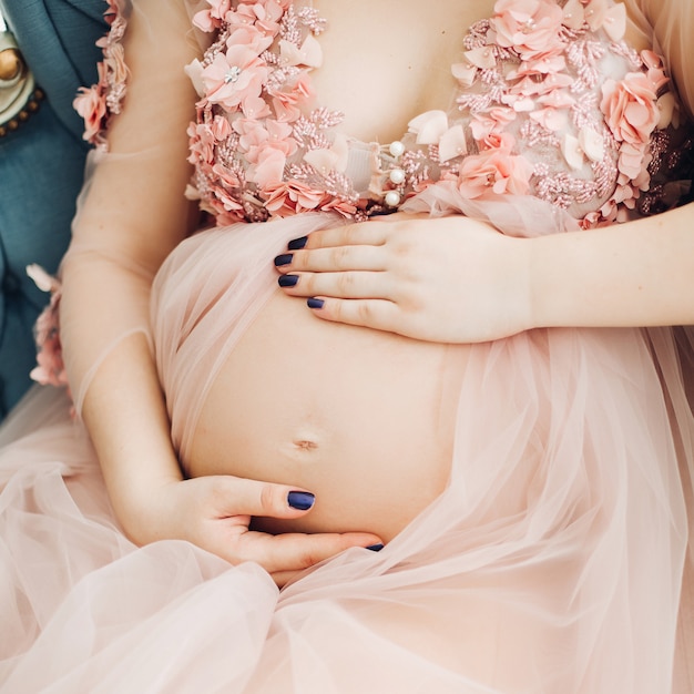 Beautiful pregnant woman holding hands on stomach at heart.