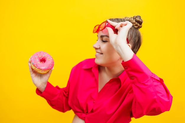 A beautiful pregnant woman holds a sweet donut in her hand on a yellow background Expecting a child pregnancy and motherhood The concept of healthy and unhealthy food diet Junk food