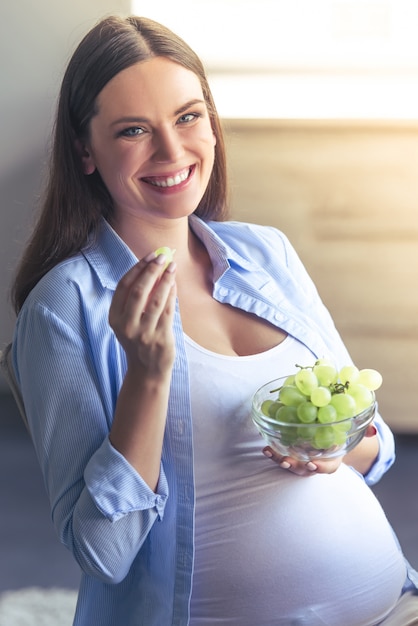 美しい妊娠中の女性はブドウを食べています。