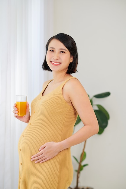 Beautiful pregnant woman is holding juice at home.