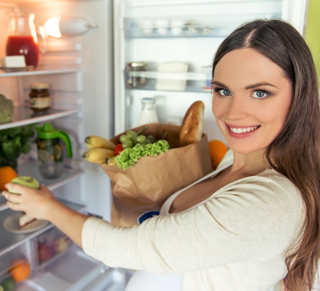 美しい妊娠中の女性は、食物と一緒に紙袋を保持しています。